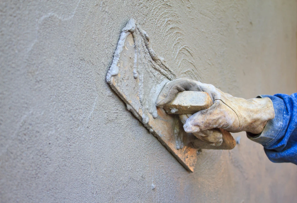 Chantier extérieur, ouvrier appliquant enduit sur mur avec taloche