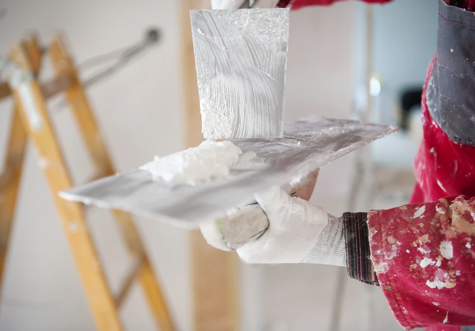 Intérieur d'un chantier de rénovation avec ouvrier appliquant un enduit ou peinture blanche au pinceau sur une surface murale