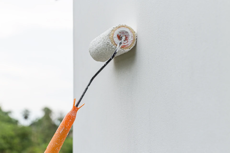 Plombier en tenue professionnelle bleue raccordant précisément deux tuyaux de cuivre avec un chalumeau sur une installation sanitaire neuve à l'intérieur d'une maison en rénovation, fixations et canalisations visibles en arrière-plan.