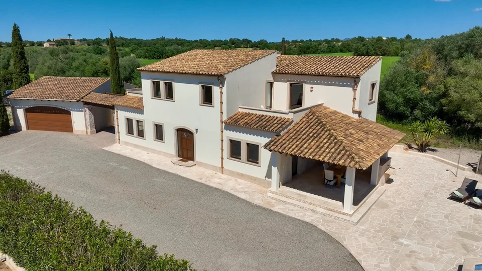 Façade rénovée d'une maison de village française à deux niveaux, enduit à la chaux taloché beige clair, soubassement en pierre de taille calcaire, volets battants bois peint vert sauge, menuiseries PVC blanc, porte d'entrée bois naturel, toiture tuiles canal, descente EP PVC, ciel bleu dégagé