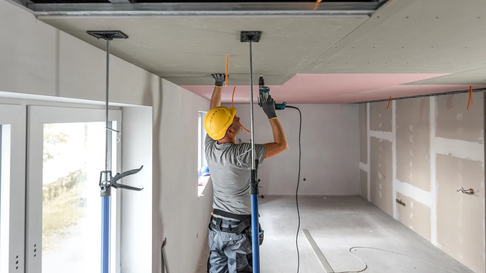 Chantier de rénovation intérieur avec ouvrier appliquant un apprêt sur mur en béton brut à l'aide d'un rouleau de peinture